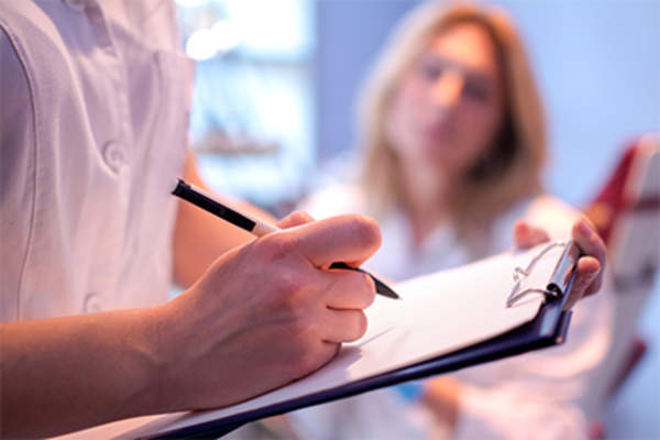 Health care provider writing in female patient's medical chart.
