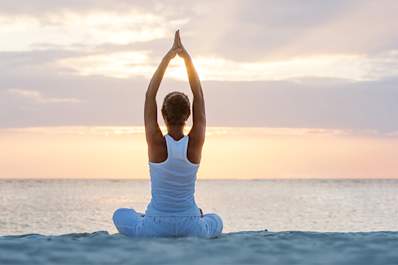 Woman doing yoga on the beach at sunrise.