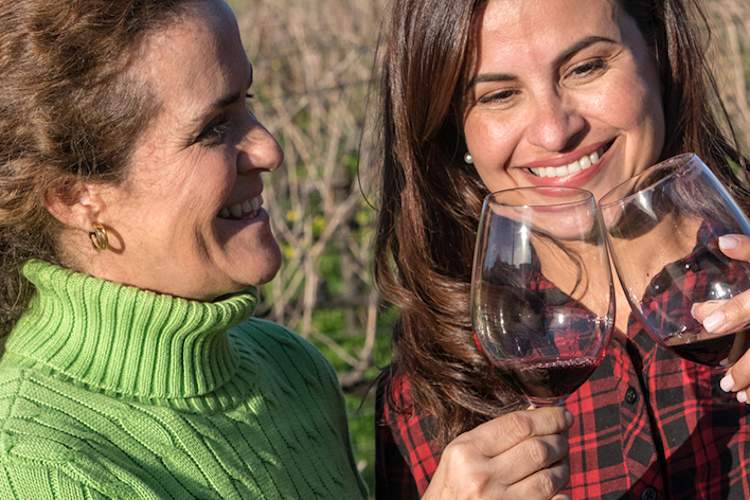 Smiling women drinking a glass of wine outside at a winery.