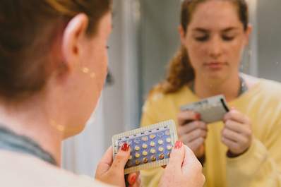 Woman looking at her sheet of birth control pills in a mirror.