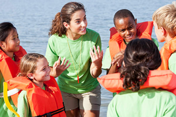 Summer camp counselor talking to children wearing life jackets.