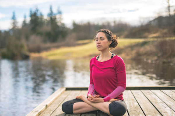 Woman meditating at lake on pier.