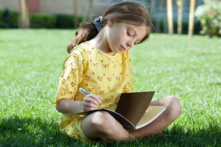 Young girl sitting in the grass writing in her journal.