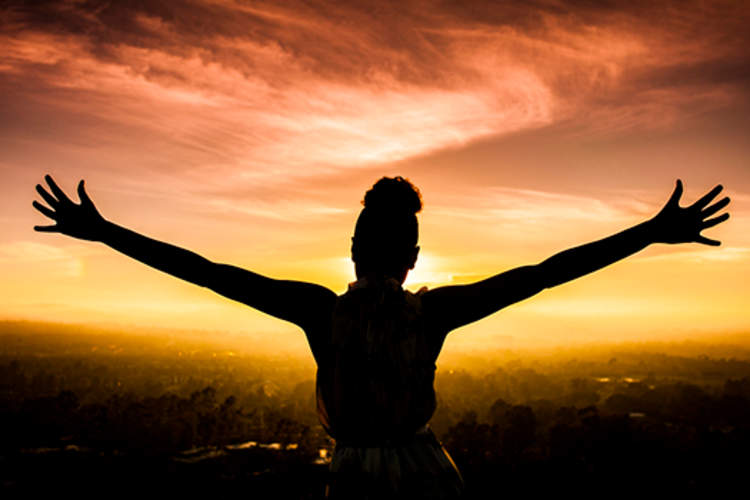 Woman staring at the sunset with her arms wide.