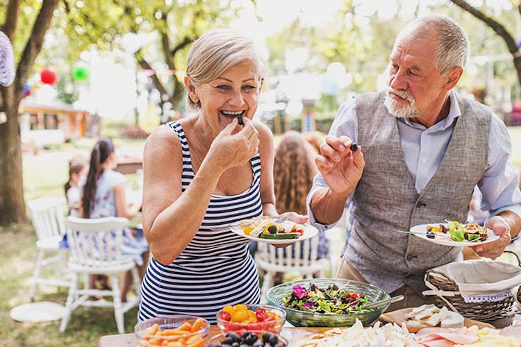 Senior couple serving a salad at an outdoor party.