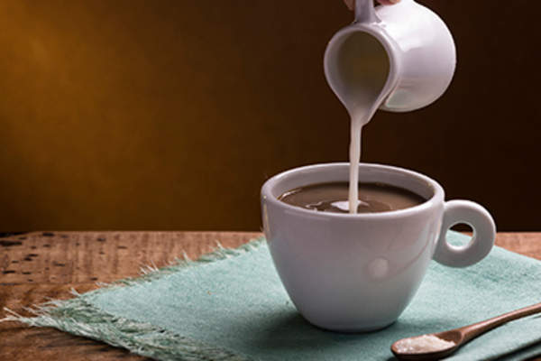 Pouring cream into a cup of coffee.
