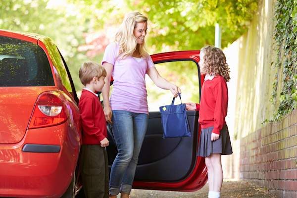 Mother and children in school uniform next to red car