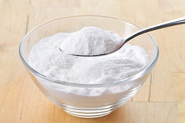 Baking soda in a glass bowl and in a spoon.