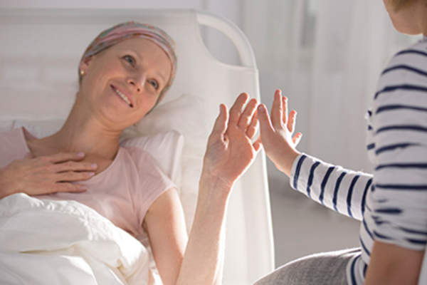Smiling woman in hospital bed touching hand to daughter's.