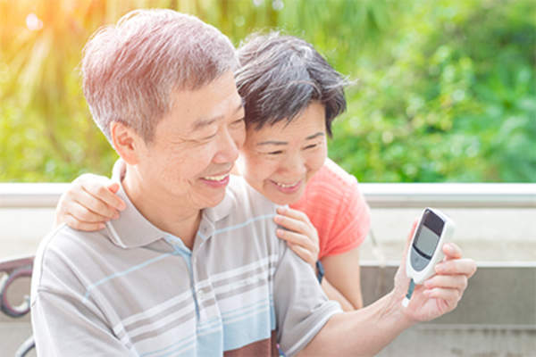 Smiling older couple checking the man's blood sugar levels.