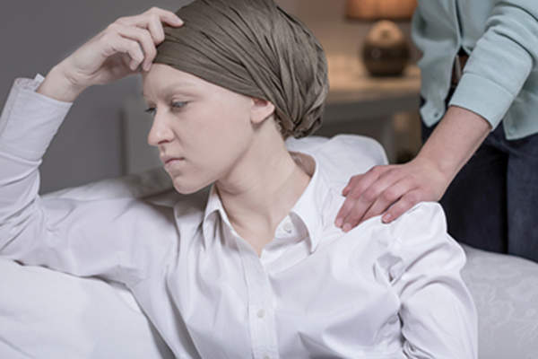 Supporting woman with cancer sitting on couch with hand on shoulder.