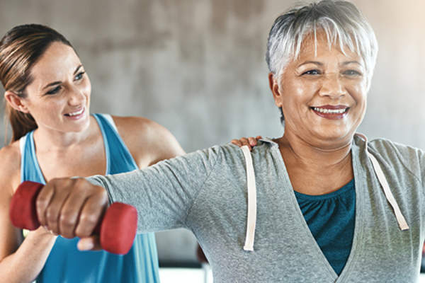 Woman lifting weights with a trainer image.