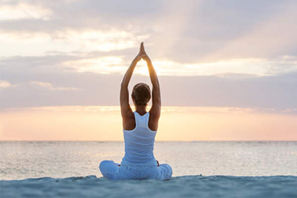 Woman practicing yoga on the beach at sunrise.