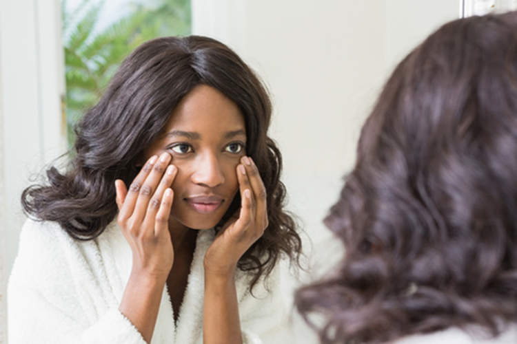 Woman checking skin on face in mirror.