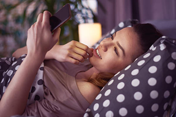 Girl laying down on bed and using smart phone.