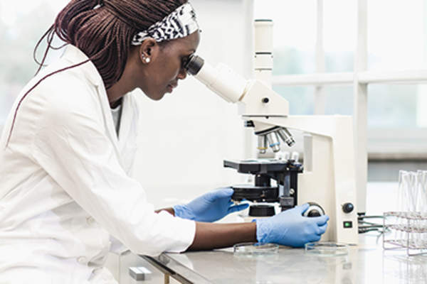 Female scientist looking in microscope in laboratory.