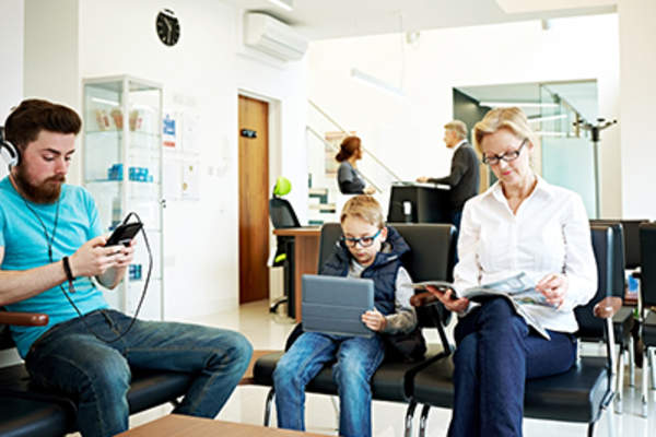 People on a phone, tablet, and laptop in waiting room.