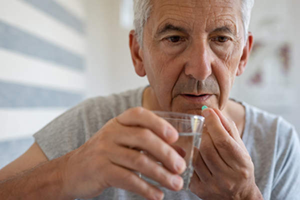 Senior man swallowing an oral agent for prostate cancer treatment.