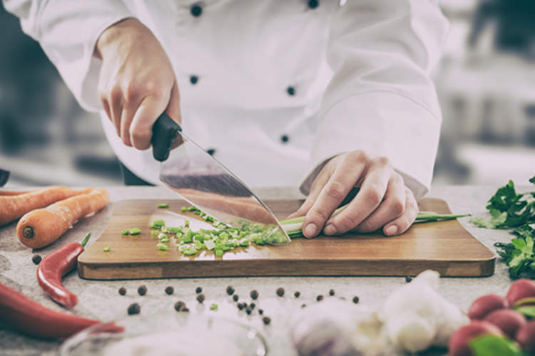 Chef chopping vegetables on cutting board.
