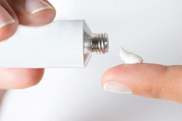 Woman putting ointment on finger to apply to skin.