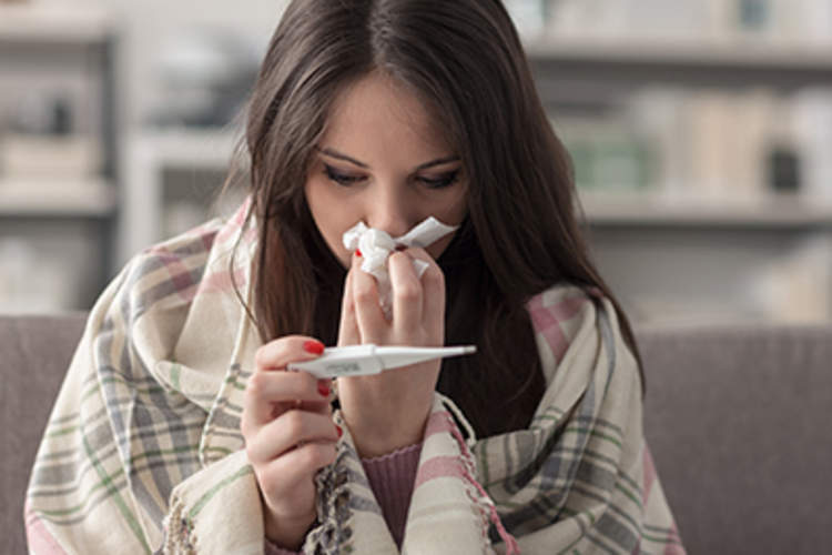 Sick woman blowing her nose and reading her temperature a thermometer.