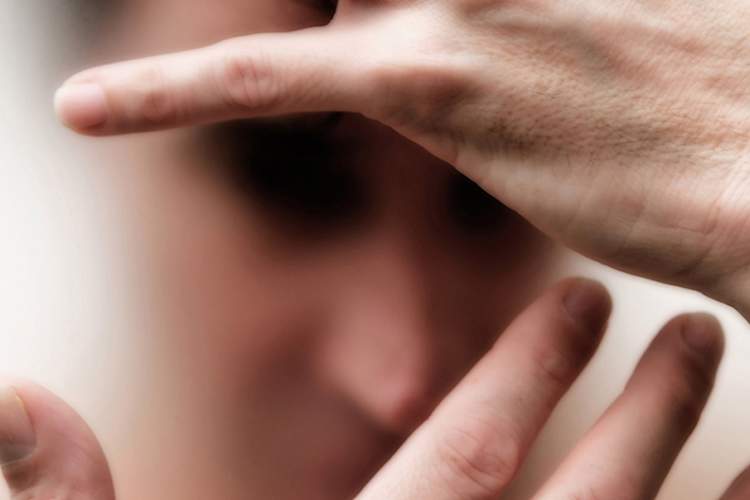 Psychosis concept, man with hands over face, blurred.