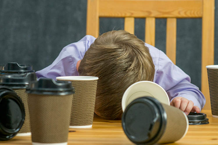 Boy asleep at the table with coffee cups around.
