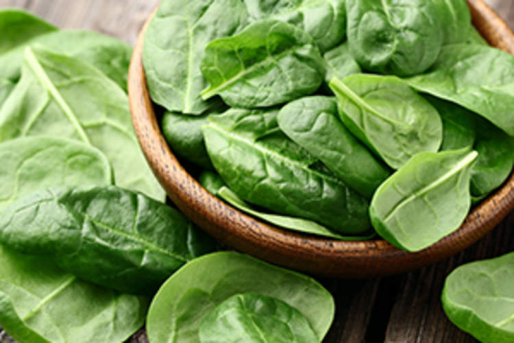 Fresh baby spinach leaves in a bowl on a wooden table