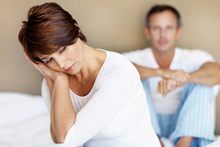 Woman distressed on a bed with a man behind her.