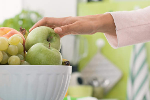 Woman taking green apple from fruit bowl.