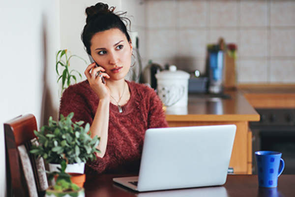 Young woman on cell phone and laptop at home.