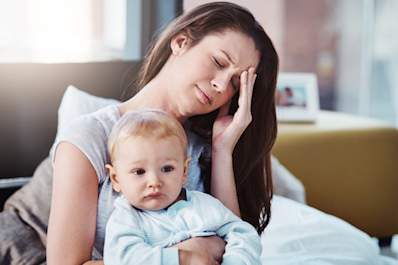 Mother sitting on bed with migraine, holding her child and her head.