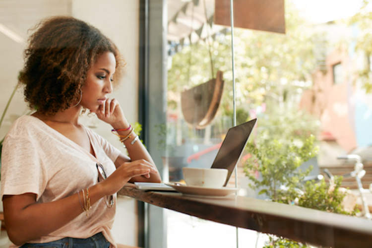 Young black woman at cafe using laptop researching CIS.