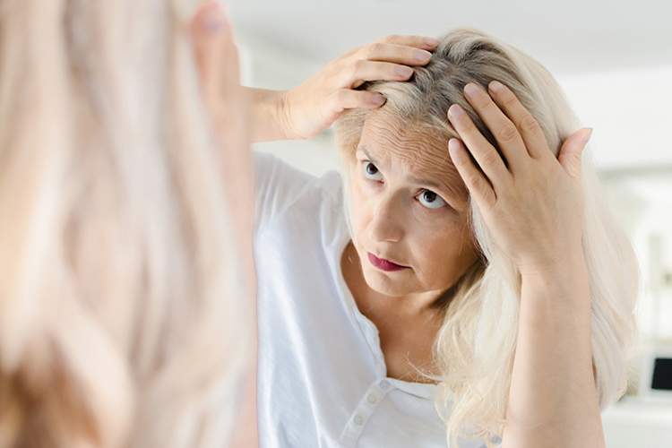 Woman examining her scalp in the mirror.