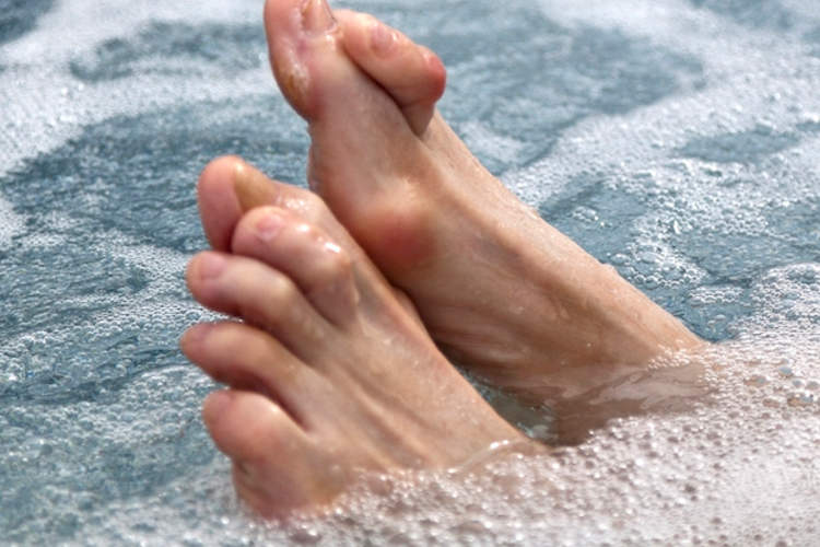 Feet with hammertoe sticking up from a bathtub.
