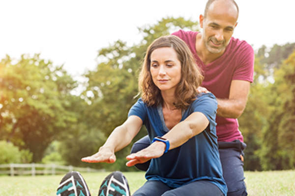 Man and woman stretching outside in park.