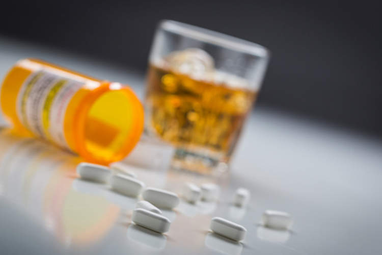 A bottle of prescription pills spilled out in front of a glass of bourbon.