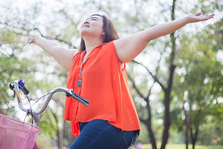 Happy, young, overweight woman on a bicycle with arms up.