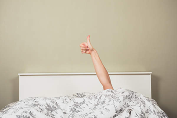 Woman under bed covers giving thumbs up.