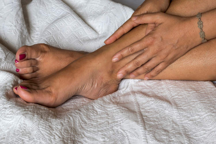 A woman sits in bed with restless legs syndrome.