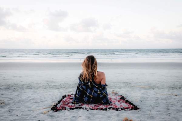 woman sitting alone on beach looking at ocean