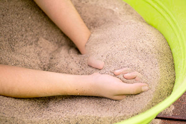 Closeup of hands enjoying and playing with sand in a bucket on a picnic table.