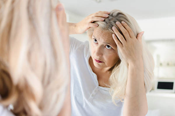 Woman examining her scalp in the mirror.