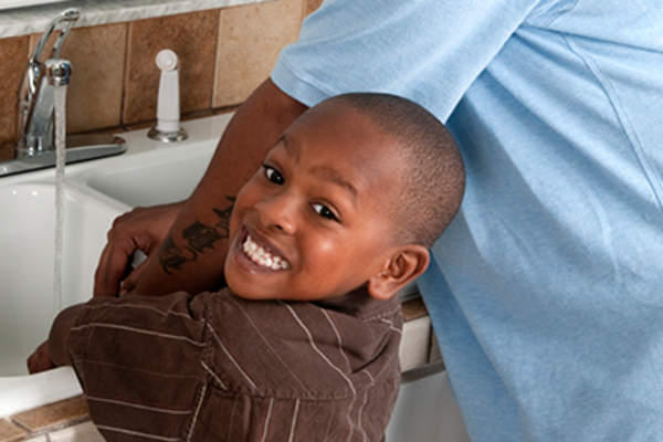 Happy young boy washing his hands with his Dad.