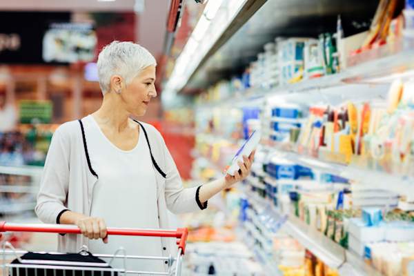 Older woman in grocery aisle holding cheese package.