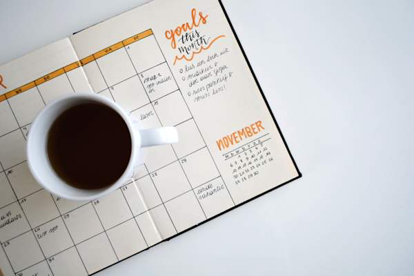 coffee mug sitting on top of day planner reading "goals for this month"