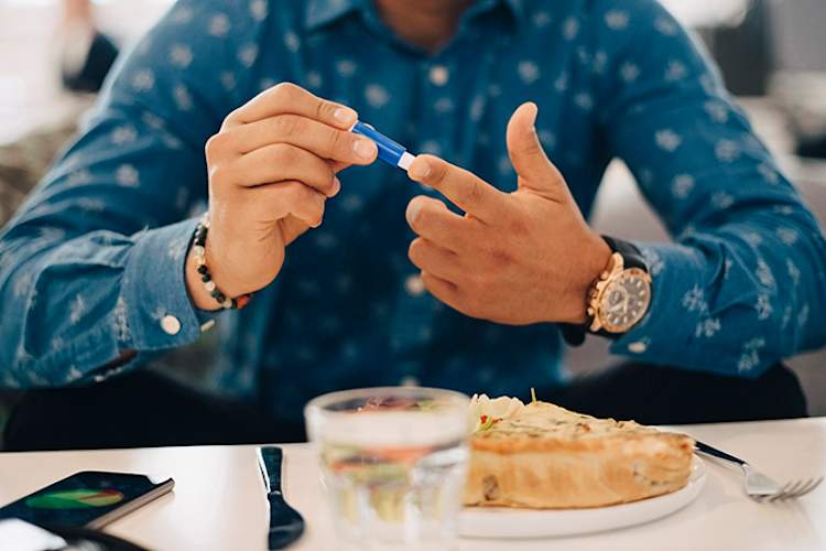 Man measuring his blood glucose and recording the information in his phone.