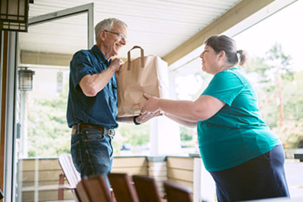Woman dropping of grocery donation to senior man.