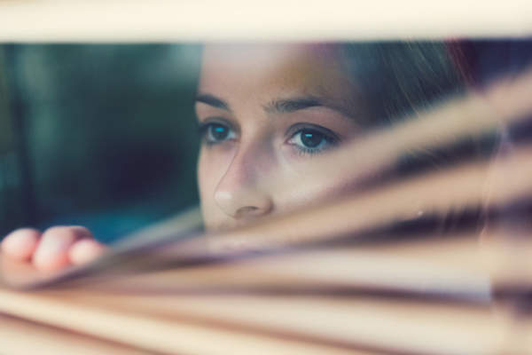 Anxious woman looking out window blinds.