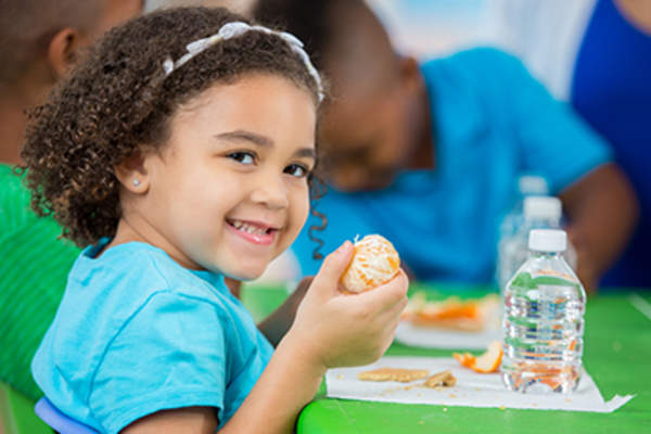 Smiling young girl eating an orange at school.